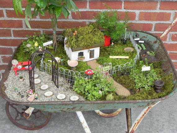 a wheelbarrow filled with lots of plants and small houses on top of it