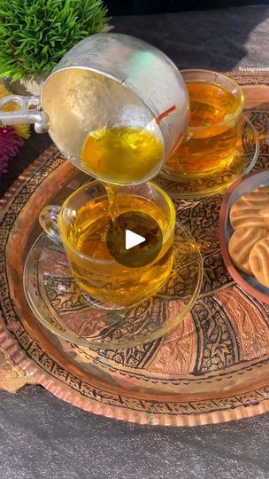 tea being poured into two cups on top of an ornate tray with flowers in the background