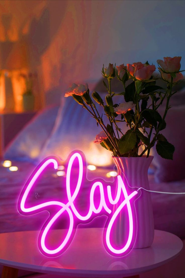 a pink neon sign sitting on top of a table next to a vase filled with flowers