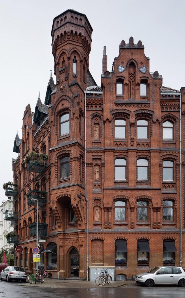 an old red brick building with many windows on the front and side, along with cars parked in front