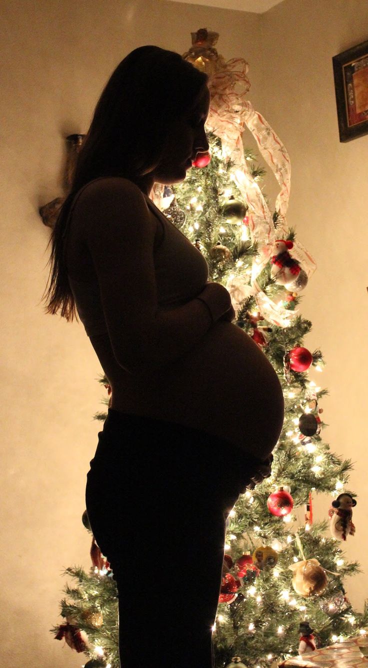 a pregnant woman standing in front of a christmas tree