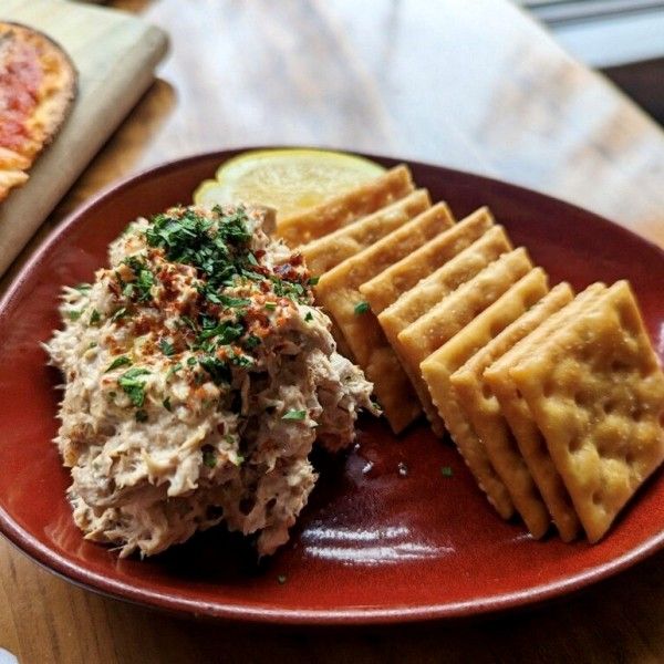 a red plate topped with crackers and food next to a slice of cheese pizza