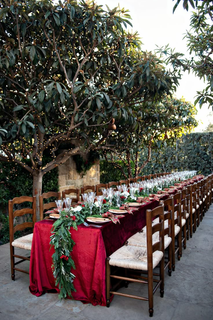 the table is set for christmas dinner with red cloths and greenery on it