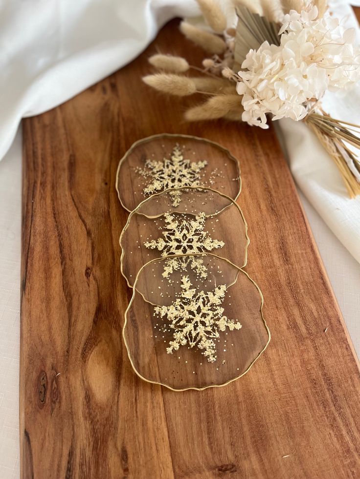 three plates with gold snowflakes on them sitting on a wooden cutting board next to dried flowers