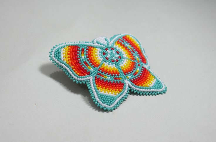 a colorful beaded butterfly brooch sitting on top of a table next to a white wall