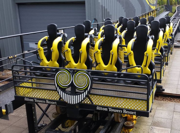 a row of yellow and black roller coasters with faces on the sides, sitting in front of a building