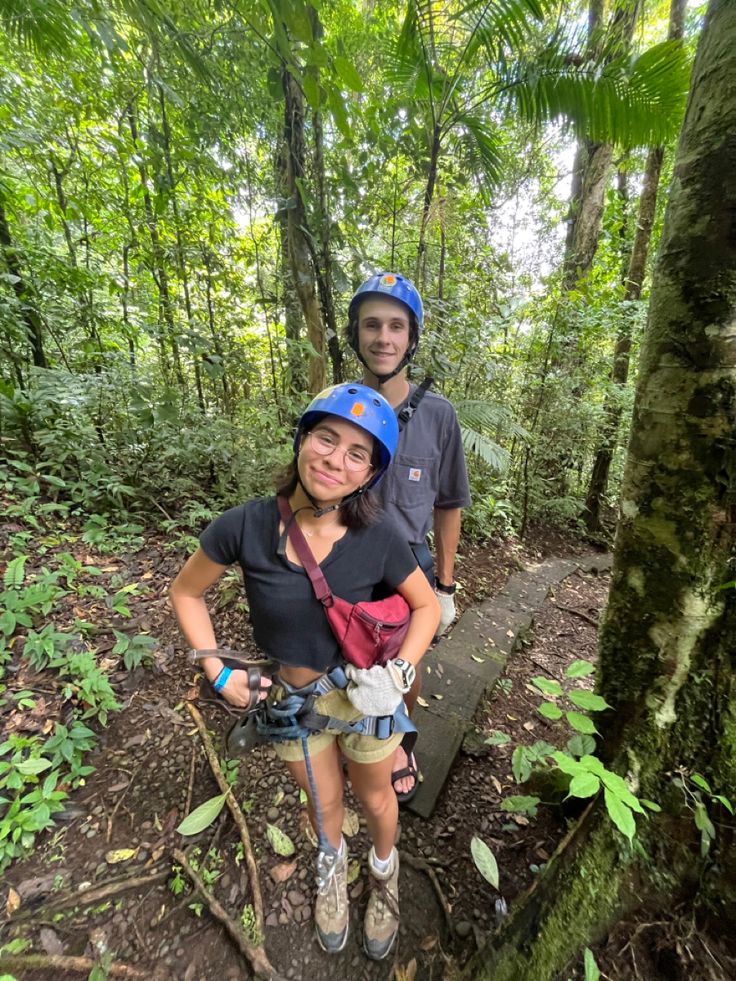 a man and woman standing in the middle of a forest with trees on both sides