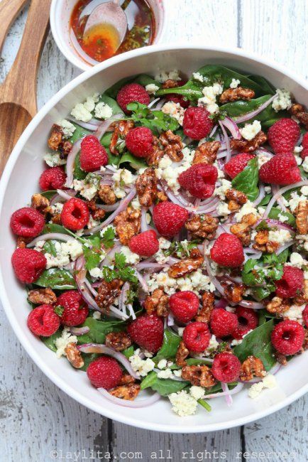 a salad with raspberries, spinach and feta cheese in a white bowl