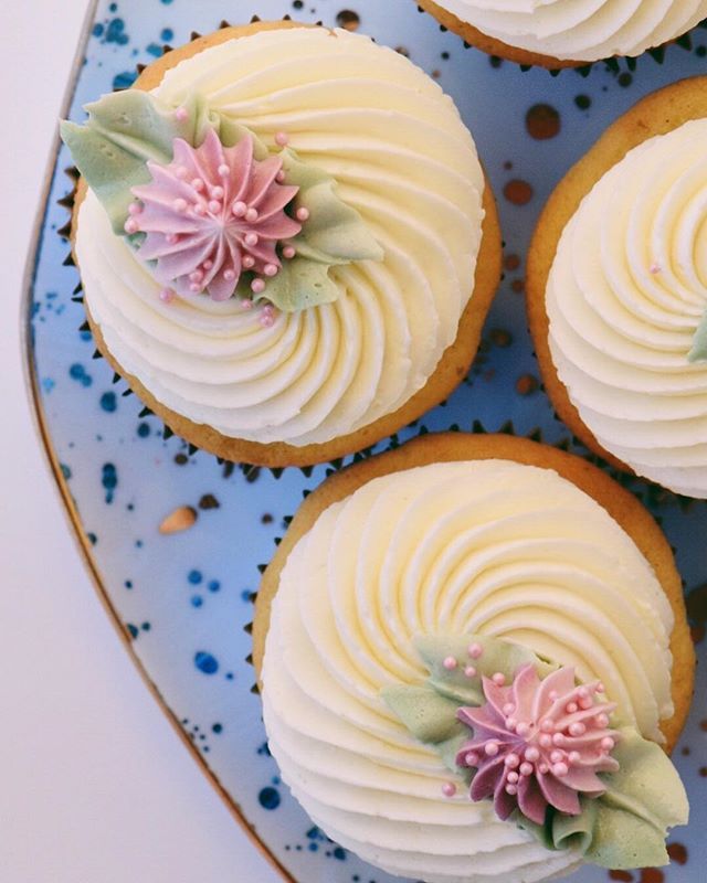 four cupcakes with white frosting and pink flowers on a blue platter