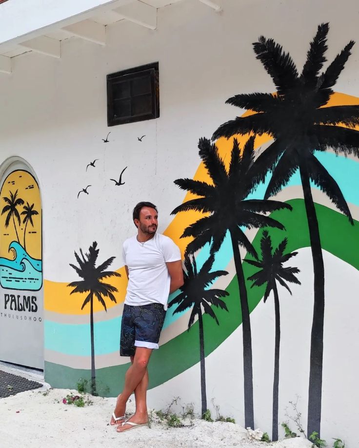 a man standing in front of a wall painted with palm trees