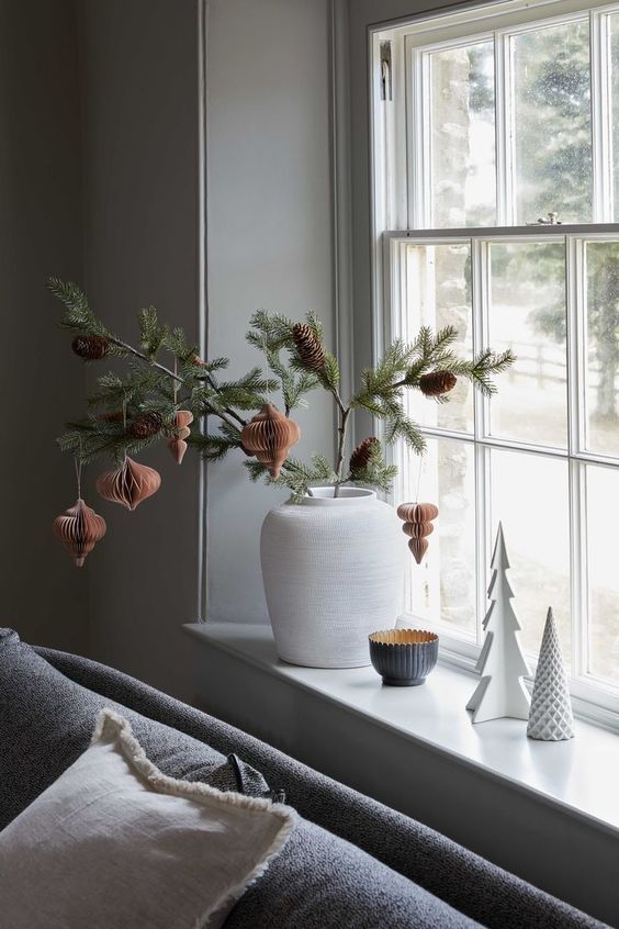 a window sill with ornaments hanging from it's sides and a potted pine tree in the foreground