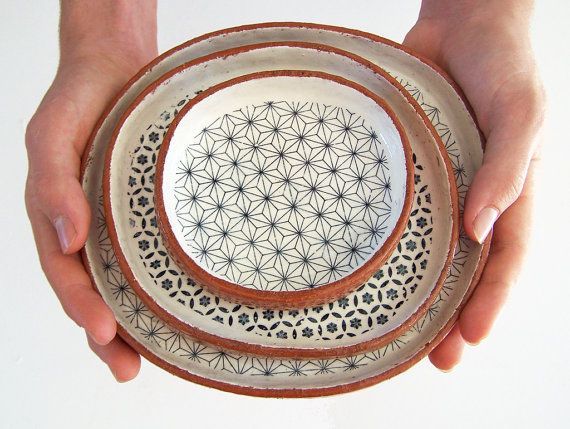 two hands holding three bowls with designs on them