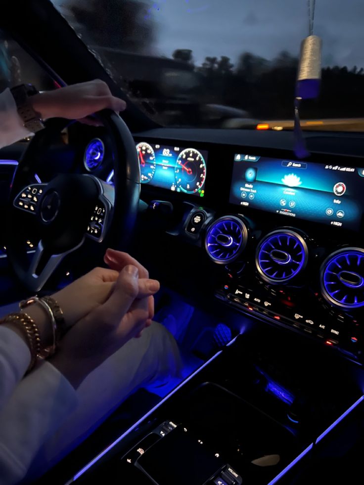 a person driving a car at night with blue lights on the dashboard and steering wheel