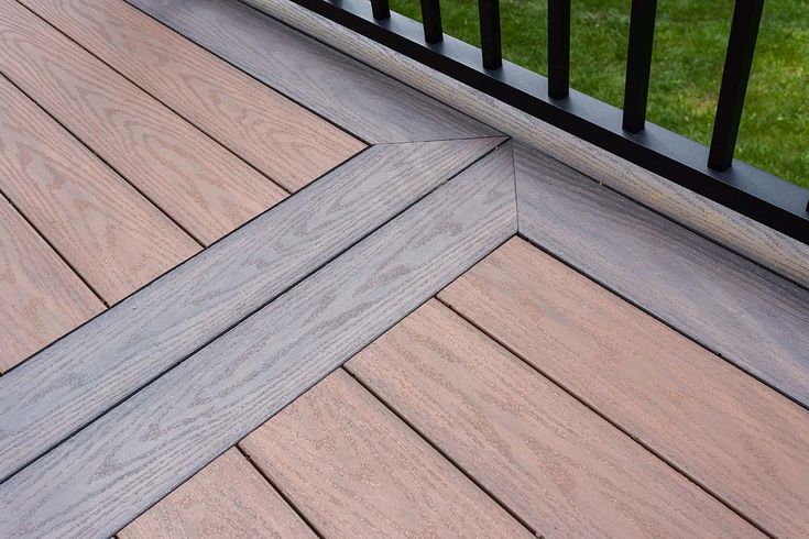 a close up of a wooden deck with black railing and green grass in the background