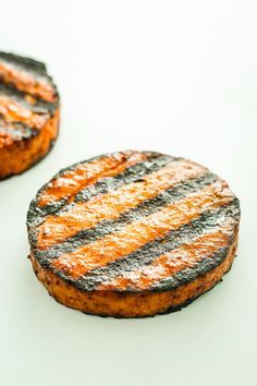 two grilled hamburgers sitting on top of a white table next to each other