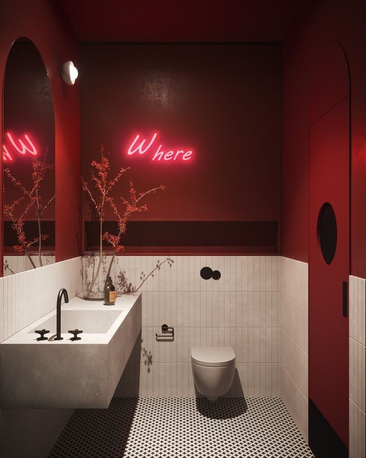 a bathroom with two sinks, a toilet and a red neon sign on the wall