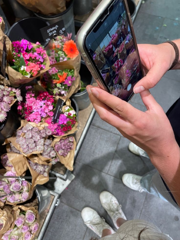 a person holding up a cell phone in front of flowers