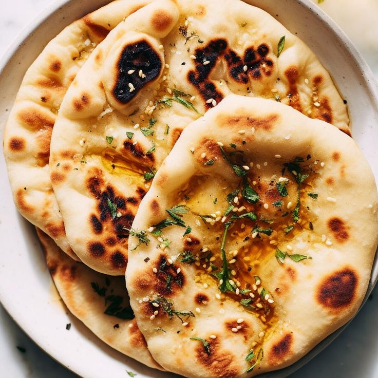 three pita breads on a white plate with herbs and seasoning sprinkles