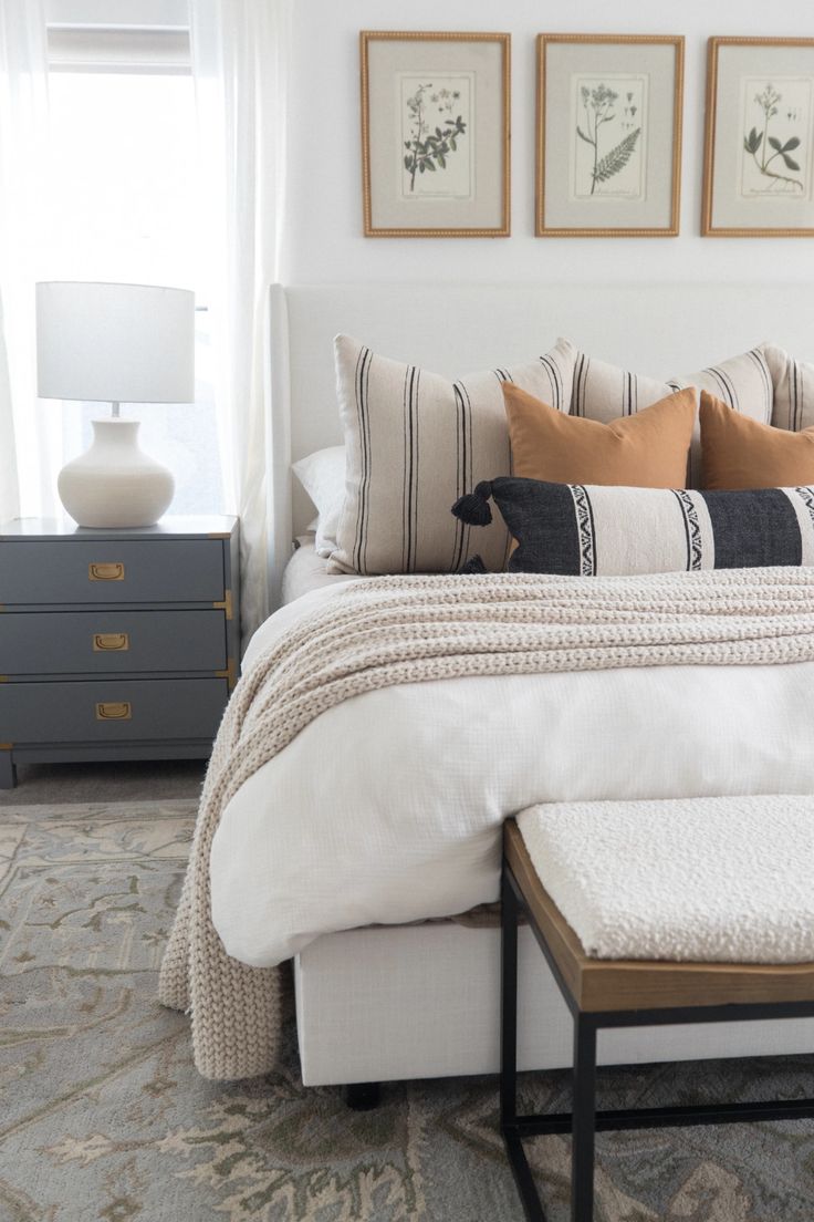 a bed with white sheets and pillows in a bedroom next to two framed pictures on the wall