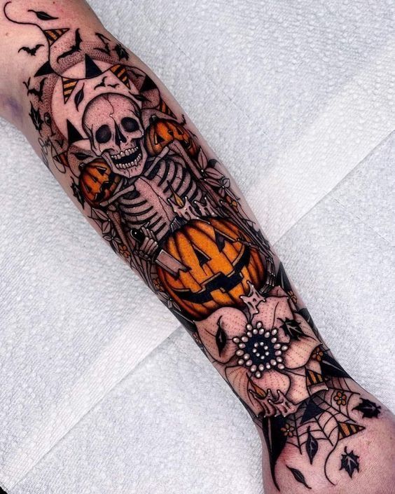 a man's arm with a skeleton and pumpkins tattoo design on it, sitting on a bed