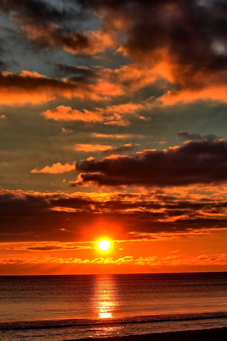 the sun is setting over the ocean with clouds