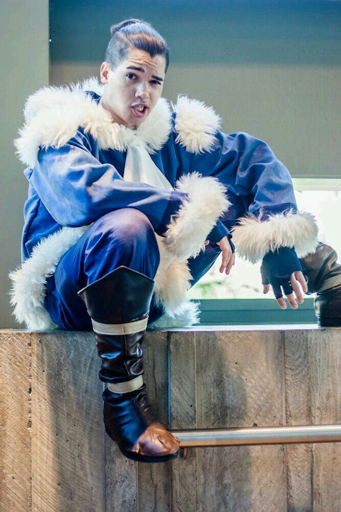 a man sitting on top of a wooden barrel wearing boots and a blue suit with white fur