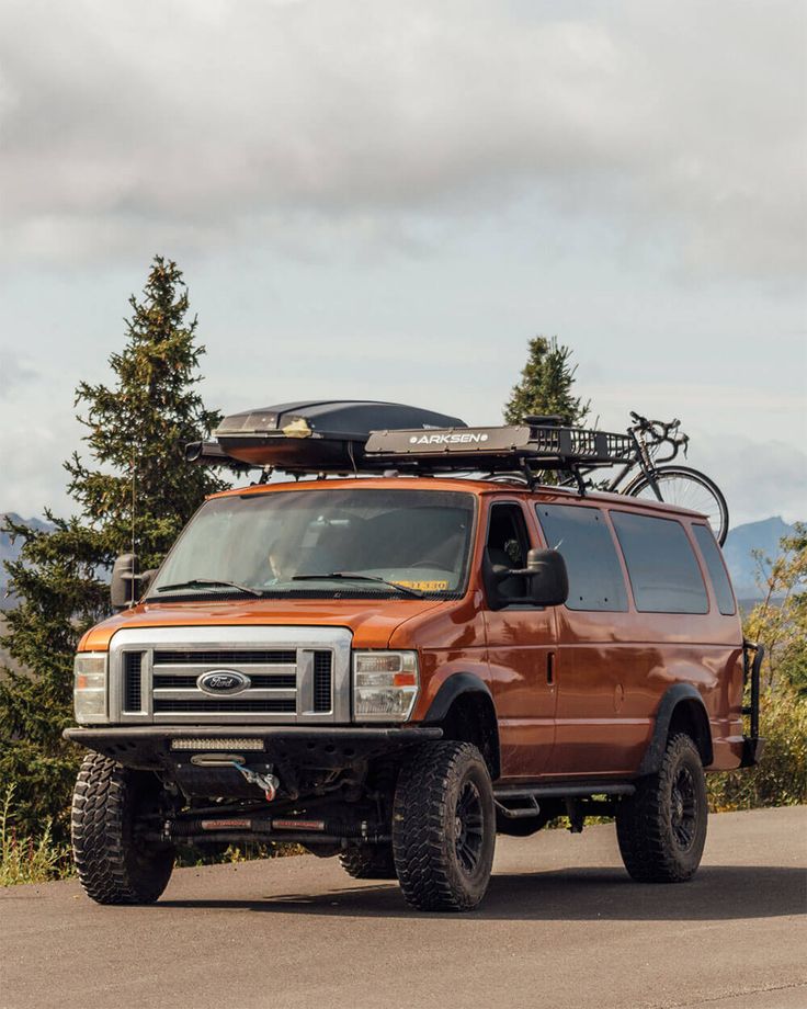 an orange van parked on the side of a road with a bike mounted to it's roof