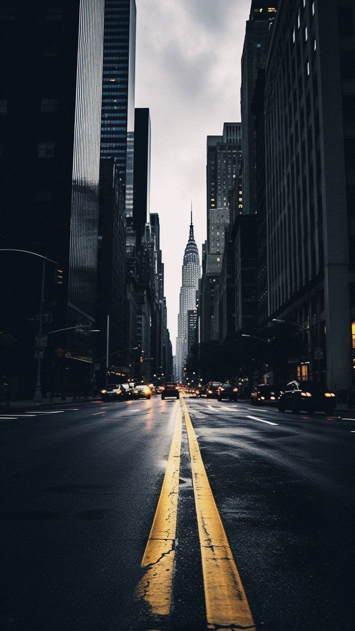 an empty city street with tall buildings on either side and yellow lines painted on the road