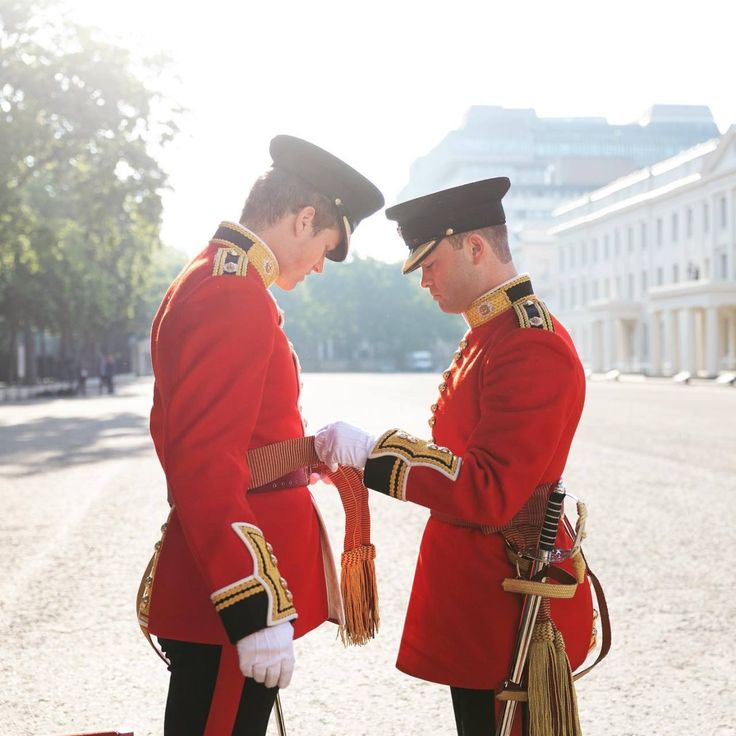 two men in red uniforms standing next to each other on the street with trees and buildings behind them