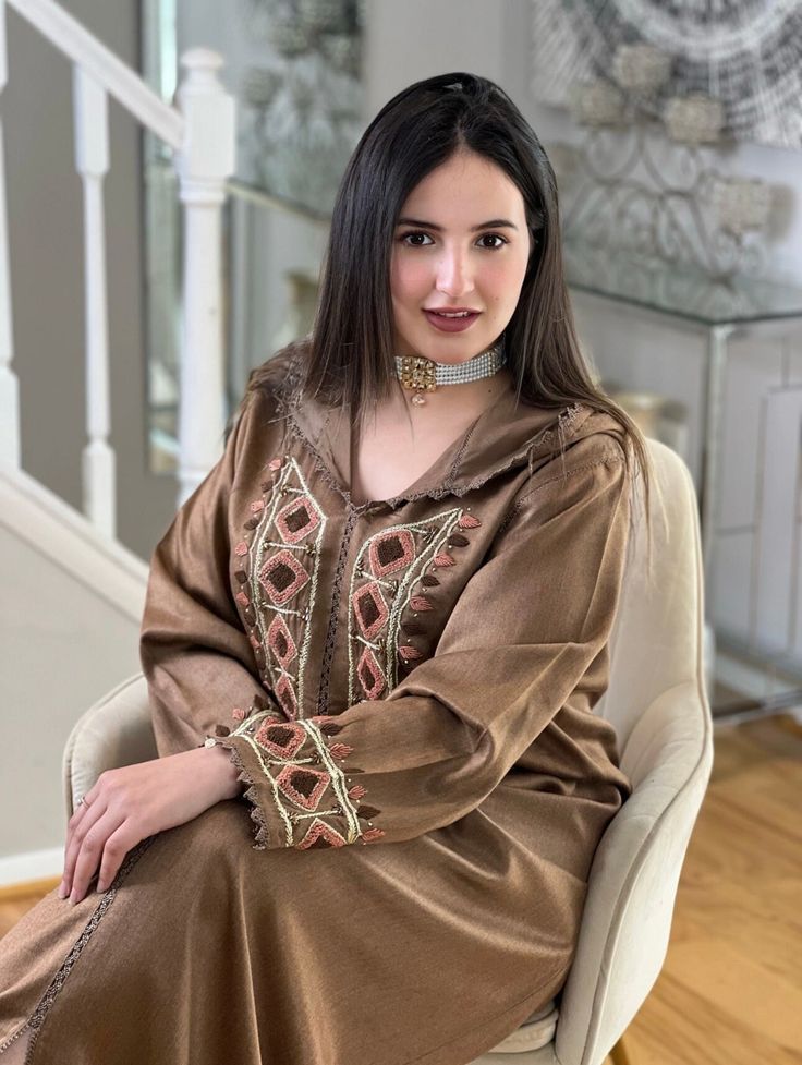 a woman is sitting in a chair wearing a brown dress with an intricate design on it