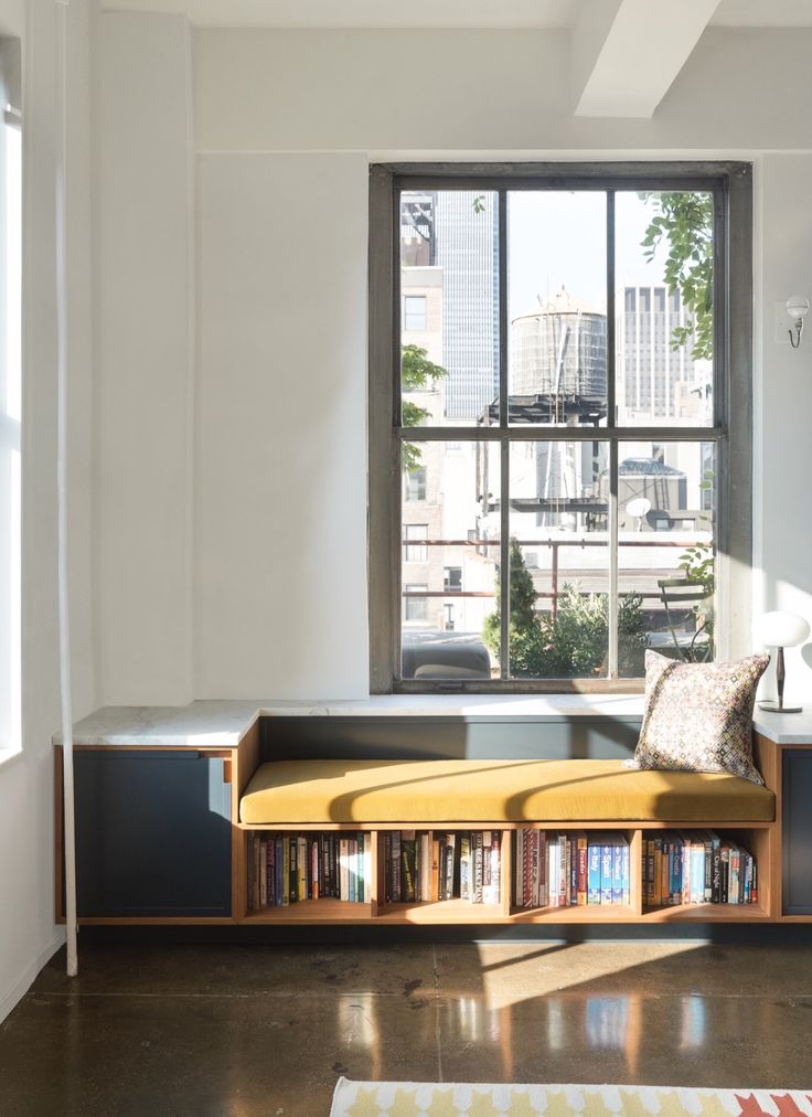 a room with a bench, bookshelf and large windows