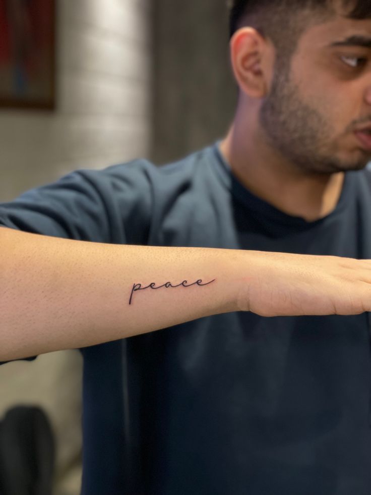 a man with a tattoo on his arm that says peace in cursive writing