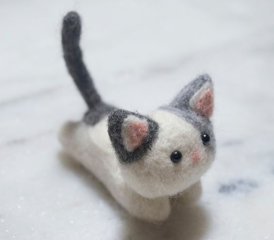 a small gray and white cat toy sitting on top of a marble counter next to a window