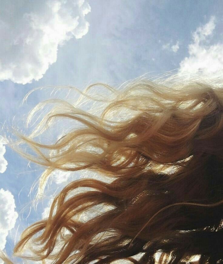 a woman's hair blowing in the wind under a blue sky with white clouds