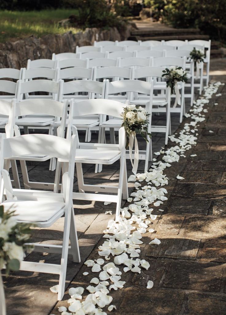 the aisle is lined with white chairs and petals on the ground for an outdoor ceremony