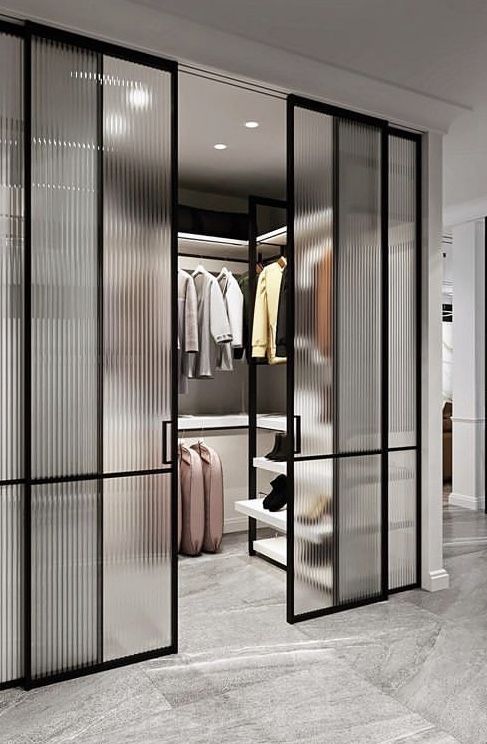 a walk in closet with glass doors and clothes hanging on the wall next to it