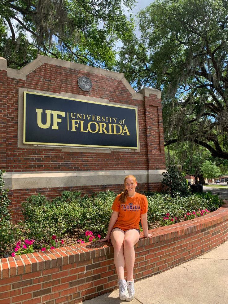 a woman sitting on a brick wall in front of the university of florida sign