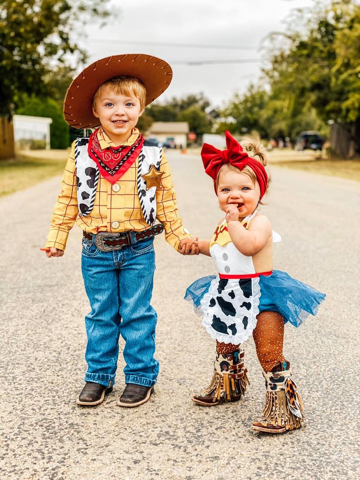 two children dressed up in costumes standing on the side of a dirt road holding hands