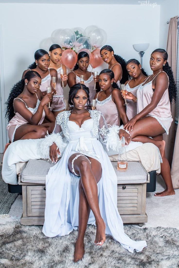 a group of women sitting on top of a bed in white dresses holding champagne flutes