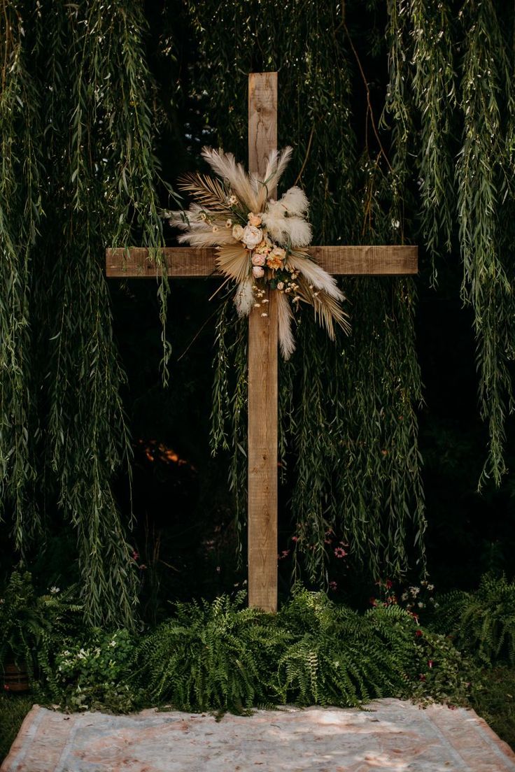 a wooden cross with feathers on it in front of some green plants and trees at night