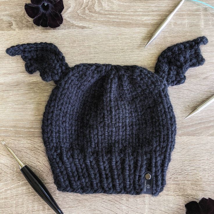 a knitted hat with ears on it next to crochet needles and flowers