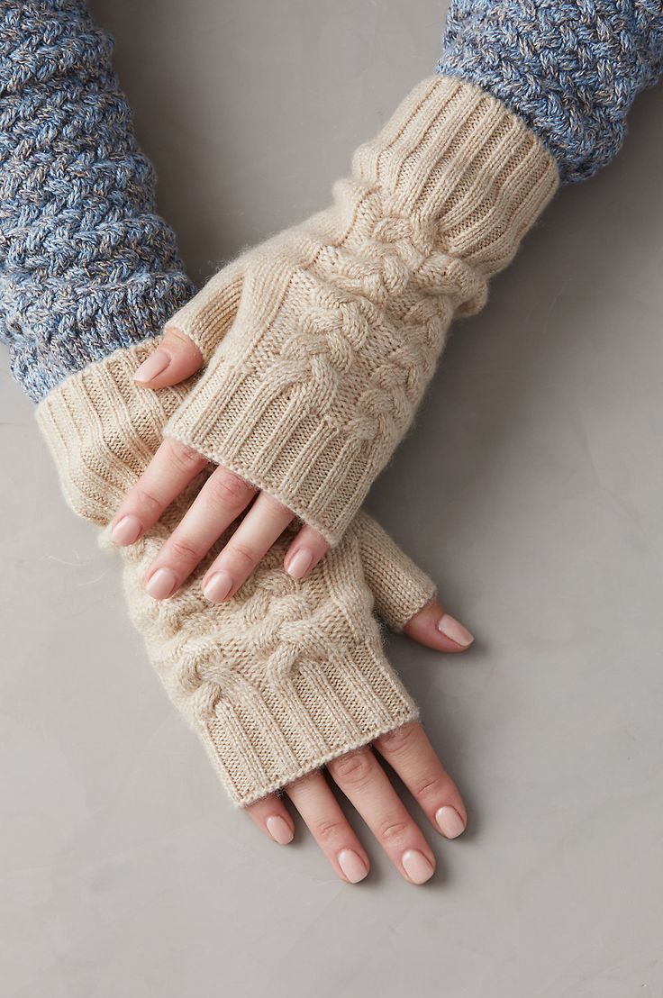 a woman's hands in knitted gloves on top of a gray surface with one hand holding the other