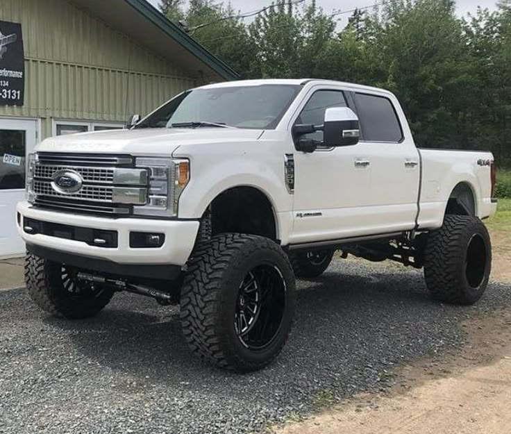 a white pickup truck parked in front of a building with large tires on it's tires