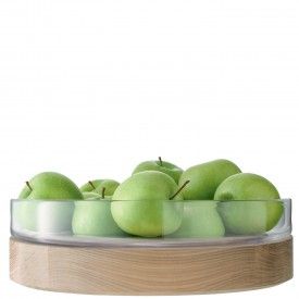 a glass bowl filled with green apples on top of a wooden table