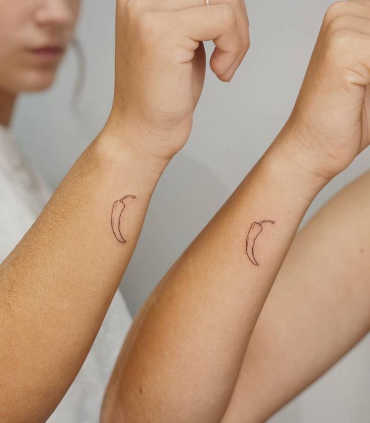 two women with matching tattoos on their arms, one holding the other's arm