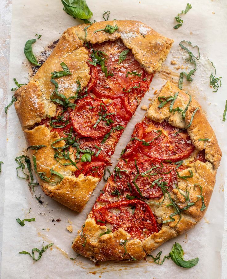 a pizza that is cut into pieces on a piece of parchment paper with basil and tomatoes