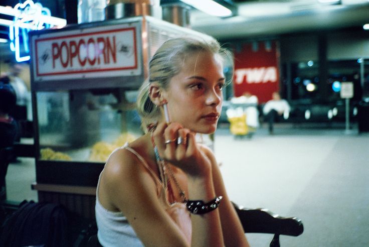 a woman sitting on a bench talking on her cell phone in an empty room with a popcorn stand behind her