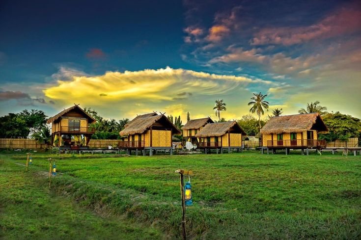 a row of wooden houses sitting on top of a lush green field under a cloudy sky