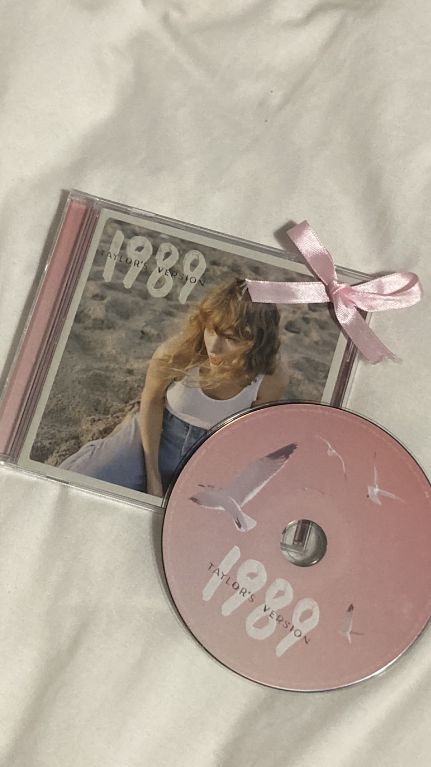 a cd with a pink ribbon around it sitting on top of a white cloth covered bed