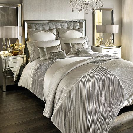 a bed with white and silver comforter in a bedroom next to a chandelier